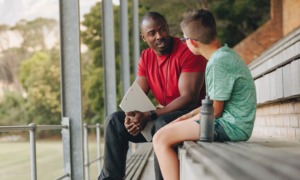 On developmental relationships _feature: black coach or mentor and white male student sit on bleachers and talk