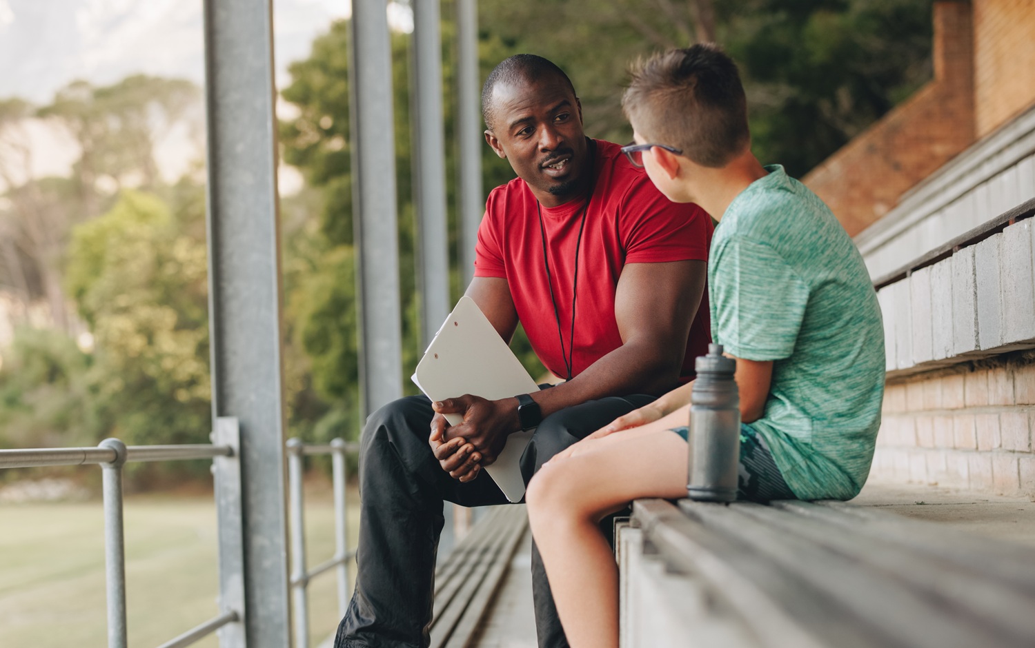 On developmental relationships _feature: black coach or mentor and white male student sit on bleachers and talk