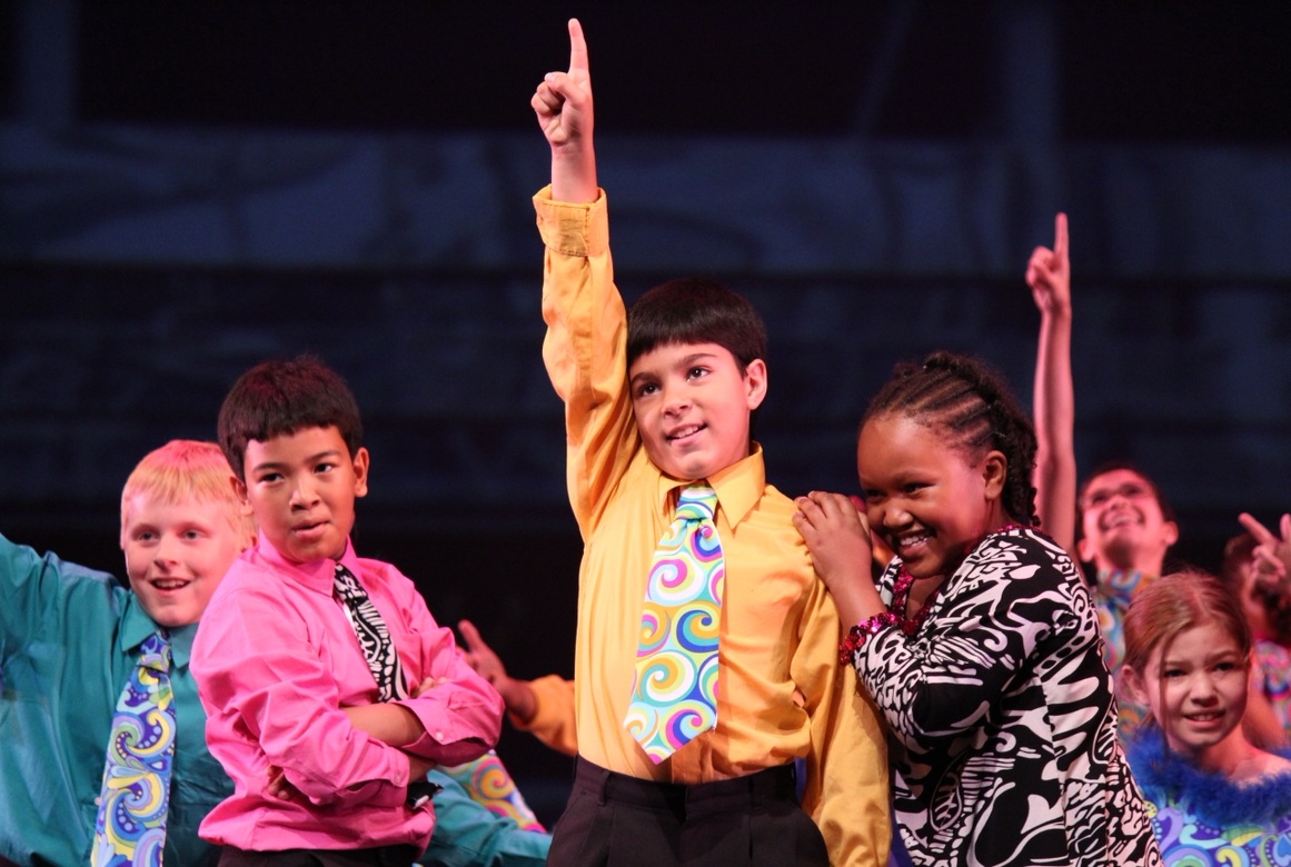 Youth dance builds the skills young people need_I credit dance with my pursuit of medicine_feature: group of children dancing on stage, some with arm raised and finger pointing up