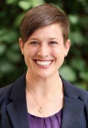 Anika Van Eaton headshot: young white woman with short hair style and blazer smiling outdoors