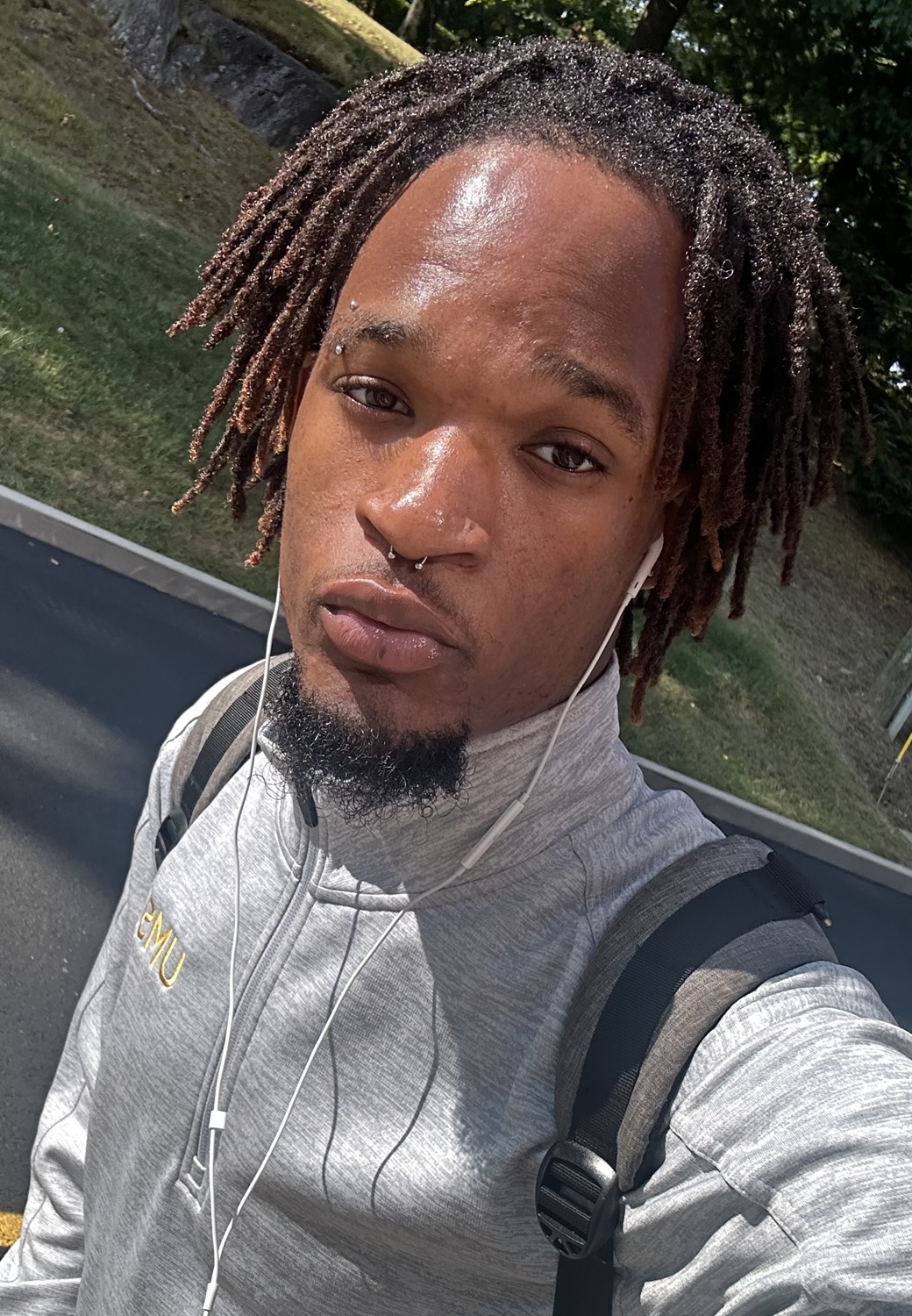 Elijah Garba headshot: young black teen with longer hair an backpack takes a selfie on the street with earphones in
