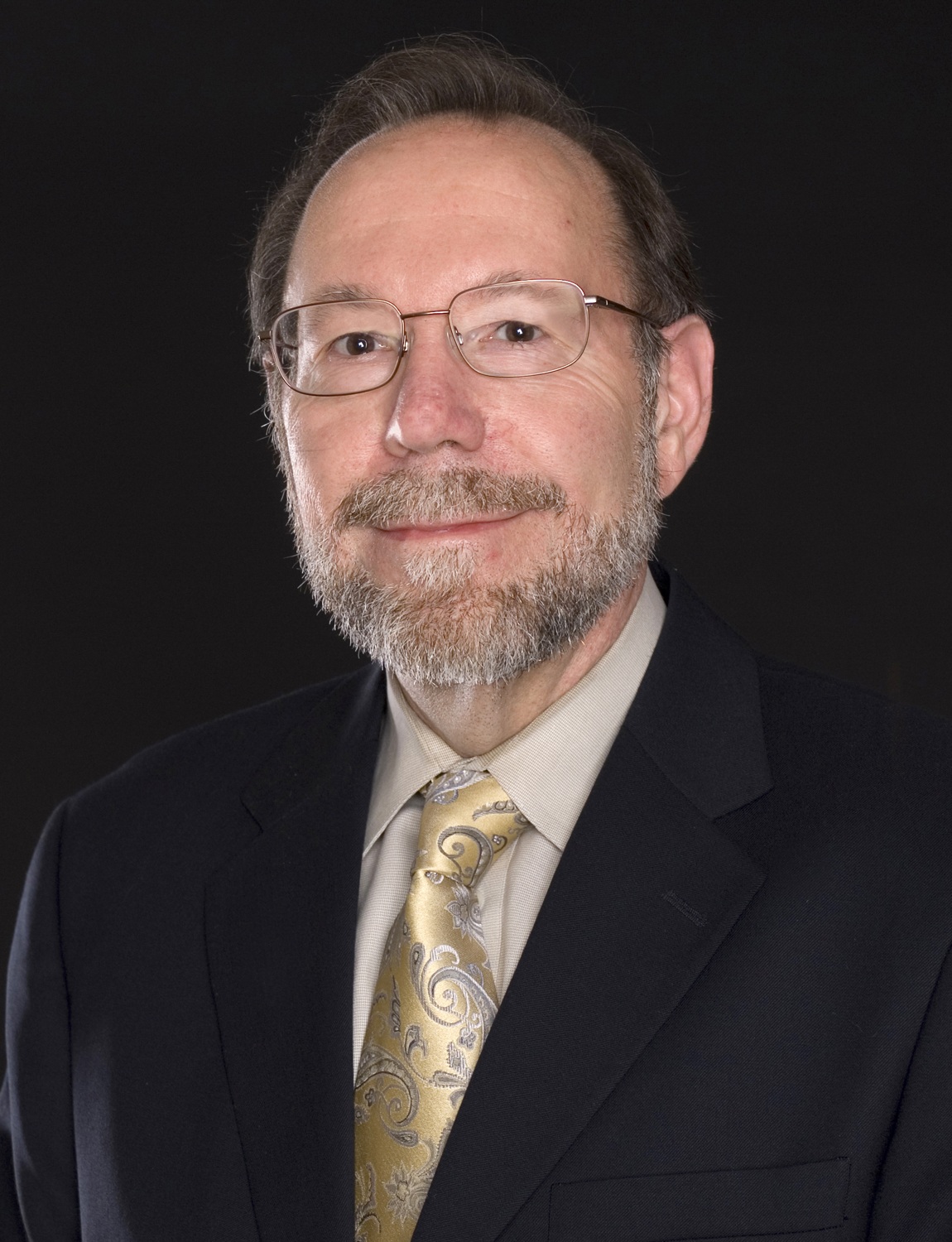 Entering the life space of the child_Frank Fecser's legacy in action_Frank Fecser headshot: older white man with glasses and beard wearing black suit and gold tie in front of black background