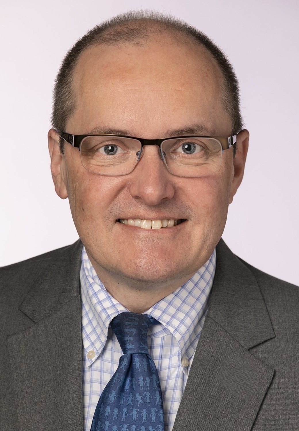 Eric Gordon headshot: white man with glasses wearing gray suit with blue tie and plaid shirt