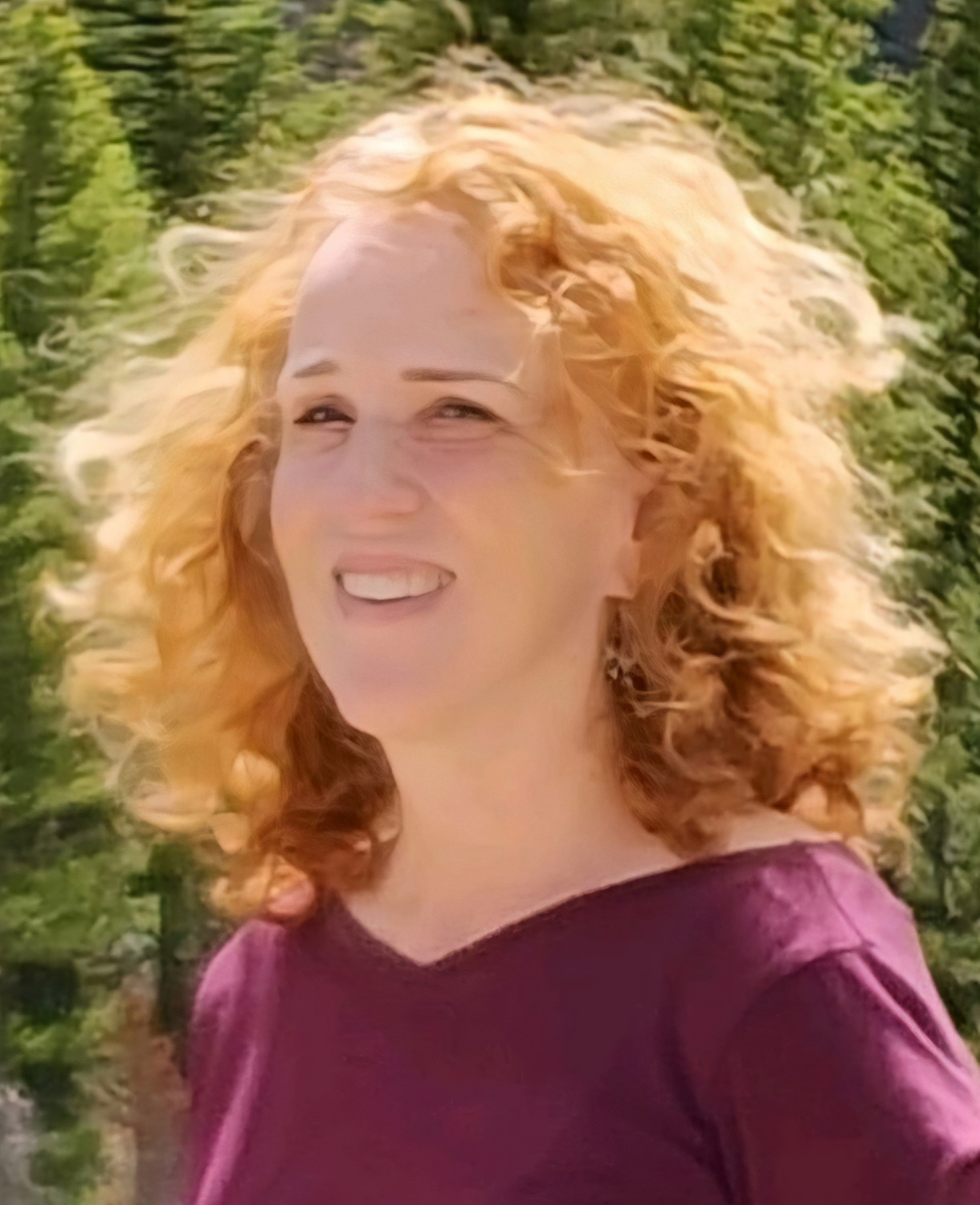 Merita Irby headshot: white woman with hair blowing in the wind and sun outdoors