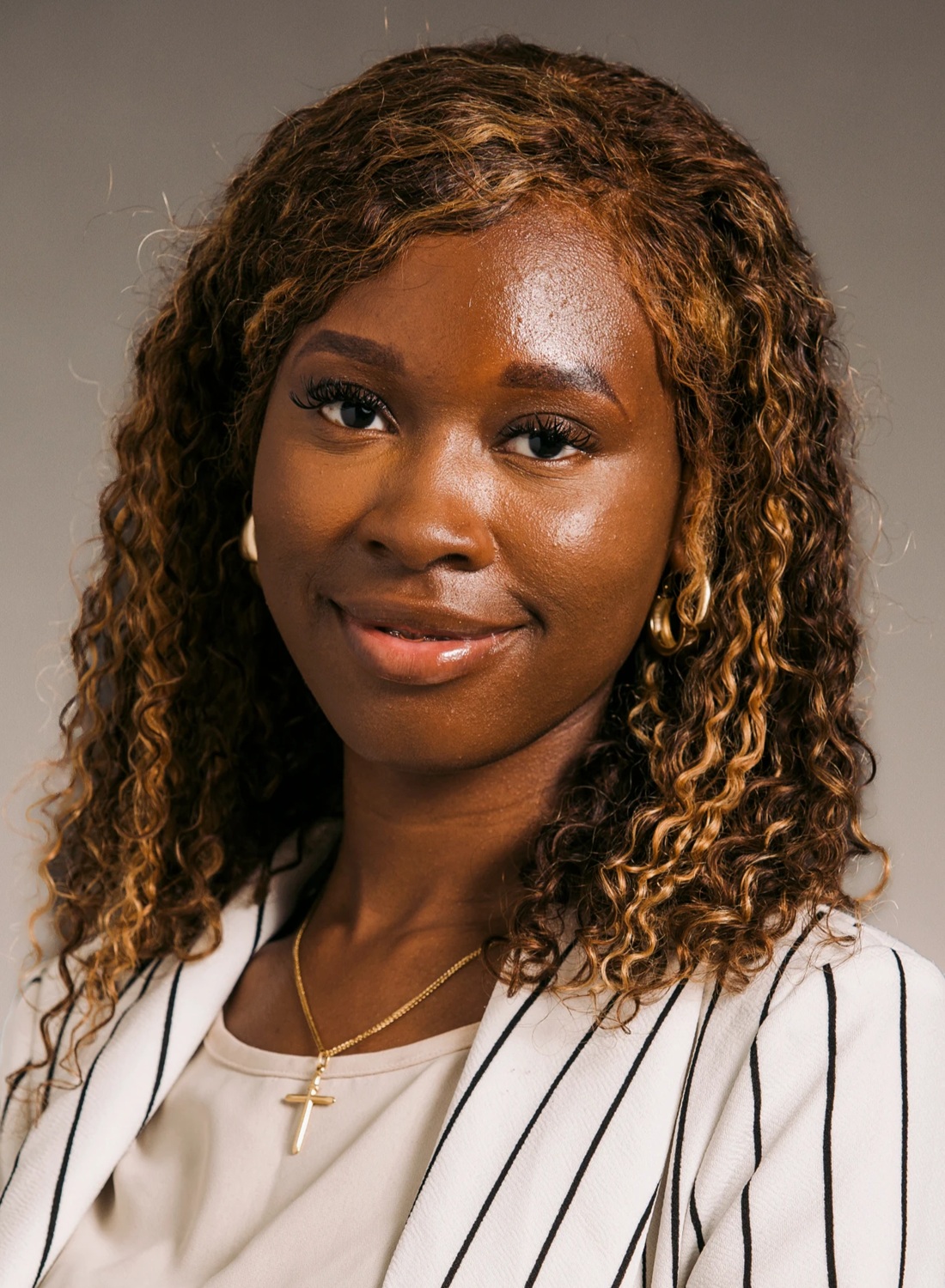 Monica-Grace Mukendi headshot: young black woman with shoulder length curly hair wearing vertical striped blazer
