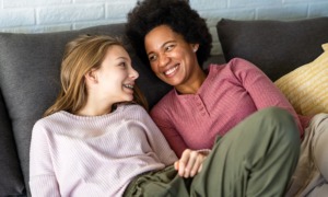 Permanency-without-connection-fails-foster-youth-True-support-means-lasting-relationships_feature: young white girl with black mom smiling at eachother on the couch