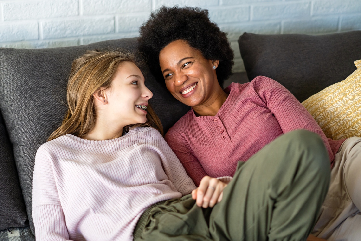 Permanency-without-connection-fails-foster-youth-True-support-means-lasting-relationships_feature: young white girl with black mom smiling at eachother on the couch