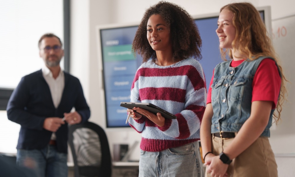 Trusting youth, We keep asking young people to trust us-But how much do we really trust them_feature: two female students giving presentation while educator looks on