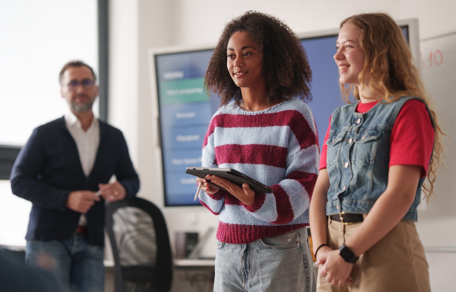 Trusting youth, We keep asking young people to trust us-But how much do we really trust them_feature: two female students giving presentation while educator looks on