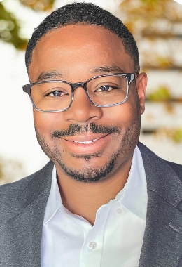 Ali Knight headshot: black man with glasses and short hair smiling wearing a blazer and button-up shirt