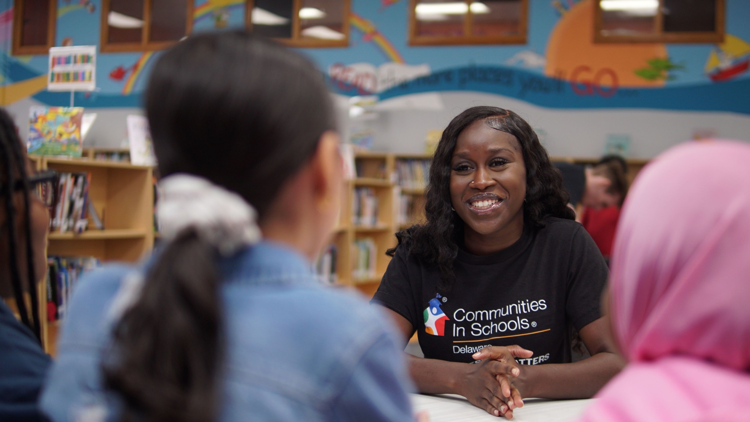 Nearly 200 student stories reveal what AI can’t replace-Relationships_Delaware: a young black woman wearing a Communities in Schools shirt talks to group of students in school library