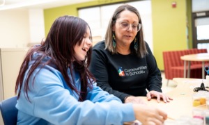 Nearly 200 student stories reveal what AI can’t replace- developmental Relationship _feature: white woman with glasses helps young girl with classwork