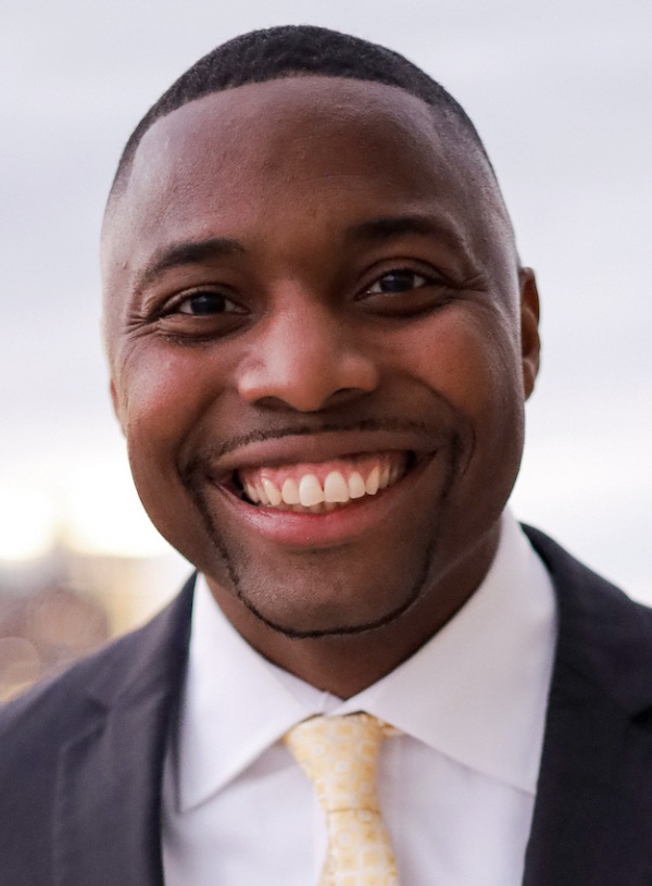 David Adams headshot: young black man in dark suit and yellow tie smiling outdoors