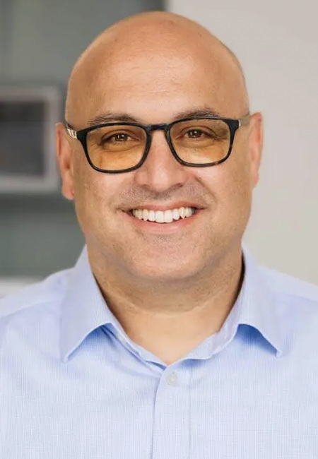 Itai Dinour headshot: bald man wearing dark-rimmed glasses and blue button-up shirt