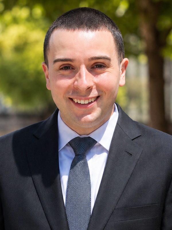 Jeffrey Vazquez headshot: young man with short dark hair wearing dark suit and tie outdoors