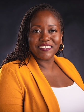 Shantalea Johns headshot: black woman with long hair wearing orange blazer with white shirt