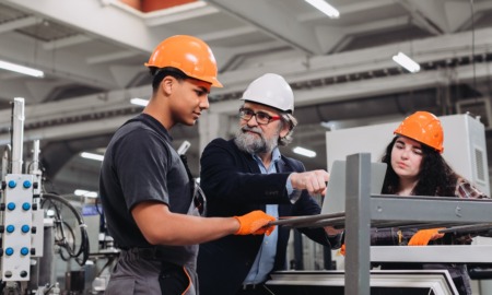 Skilled trades training and capacity-building program grants: older tradesman teaches young male and female in training on factory floor