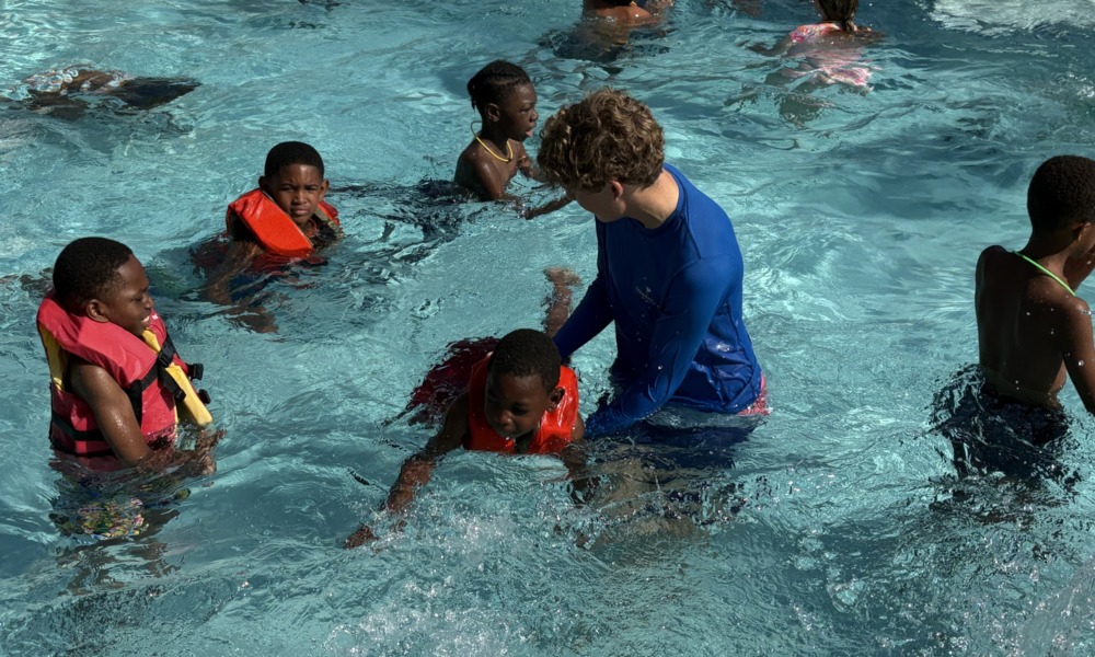 The 15-year-old behind Florida's new bipartisan drowning prevention law_feature, youth-led initiative : white teen male helps several black children in learn to swim in swimming pool