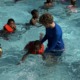 The 15-year-old behind Florida's new bipartisan drowning prevention law_feature, youth-led initiative : white teen male helps several black children in learn to swim in swimming pool