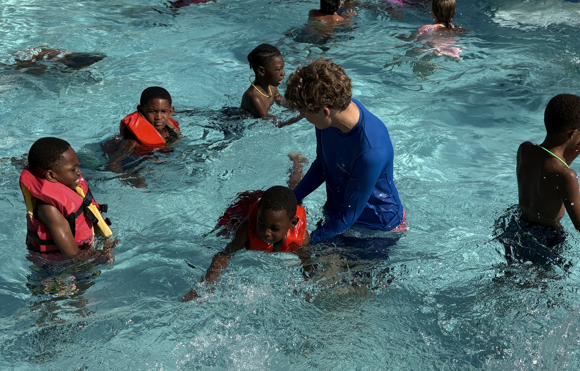 The 15-year-old behind Florida's new bipartisan drowning prevention law_feature, youth-led initiative : white teen male helps several black children in learn to swim in swimming pool