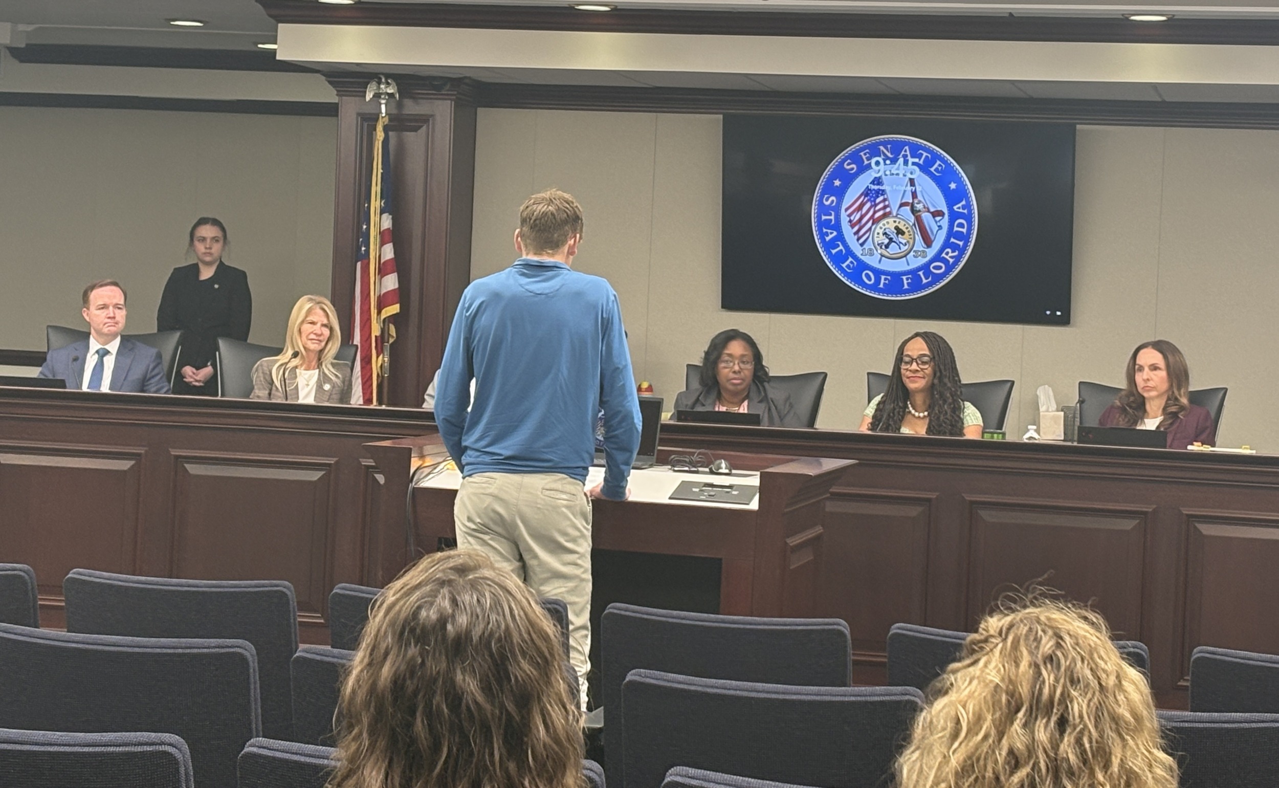 The 15-year-old behind Florida's new bipartisan drowning prevention law_presentation: a back view of young white man standing in front of legislative body giving a presentation
