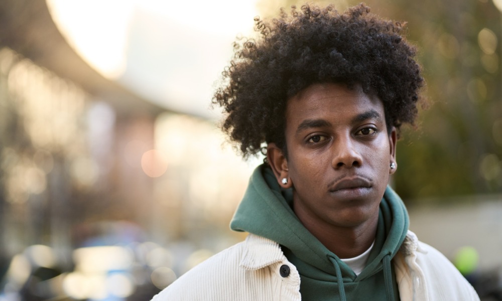 Young people aren't losing trust-they're giving up_feature: young black man in hoodie and jacket outdoors looking sad and disappointed