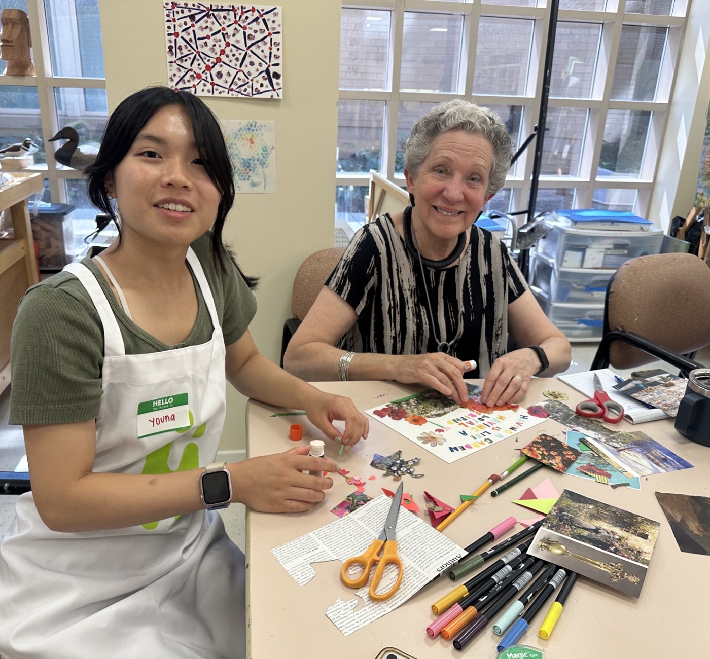 Youth development’s missing link-Intergenerational connection_activity: young Asian woman sits with older white woman at table doing arts and crafts