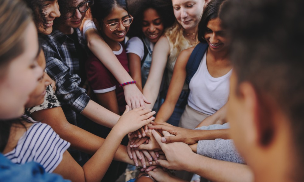 thriving youth, no youth thrives alone_feature: group of diverse teens putting hands together in group