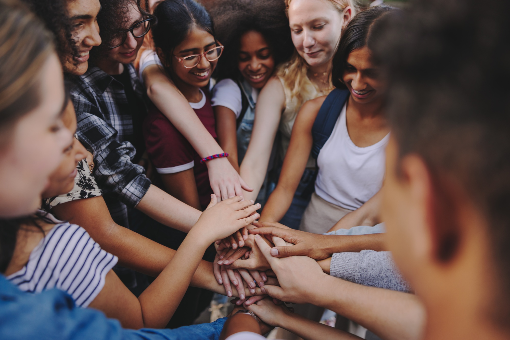 thriving youth, no youth thrives alone_feature: group of diverse teens putting hands together in group