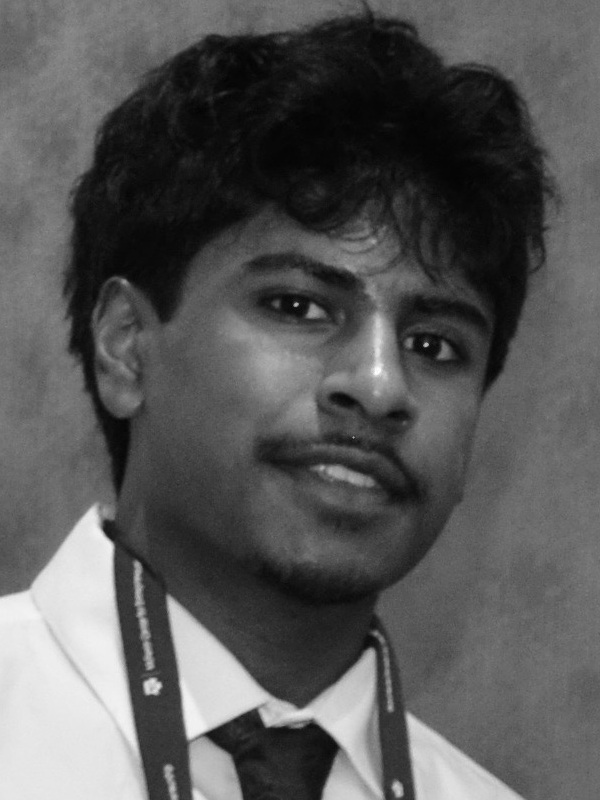 Shourya Kancharla headshot: young man with mustache wearing dress shirt and tie with lanyard around neck