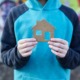 Youth homelessness prevention starts long before a young person loses their home_feature: photo of boy holding a cardboard cutout of a home