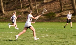 Youth lacrosse program grants_feature: teenage female lacrosse players and referee running across lacrosse field while playing