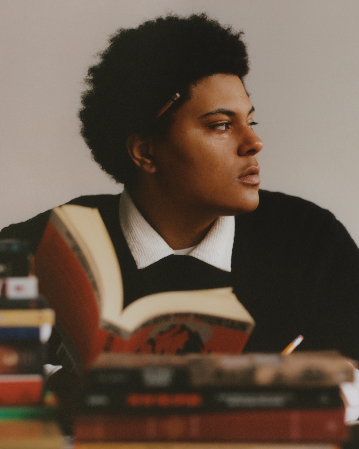 Brit Christopher headshot: person with short dark hair looks off to the side while holding a book