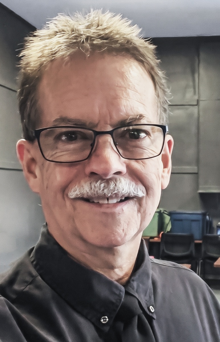 Jim Still-Pepper headshot: white man with mustache and glasses takes a selfie indoors wearing collared shirt