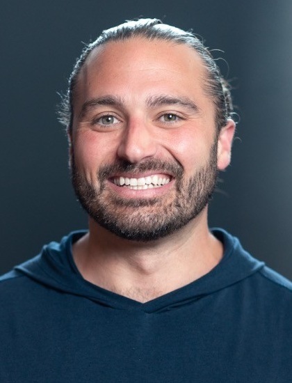 Kenneth Stivers headshot, financial education : man with pulled back hair wearing dark bluish hoody againt gray background