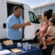 AANHPI community grant: man hands a bag to mom and daughter at community help event