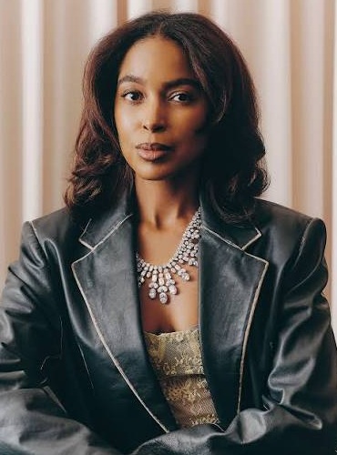 Carolyn Gray headshot: black woman with shoulder-length dark hair wearing leather jacket and intricate necklace sitting against vertical-striped background