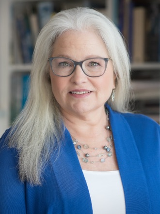 Colleen Shaddox headshot: woman with long white hair wearing glasses and blue blazer with white undershirt