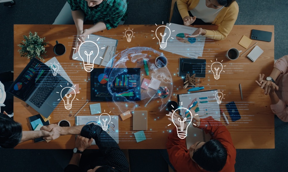 Educational leadership innovation grants: top-down view of group of people collaborating at table with lightbulb and globe graphics overlaid