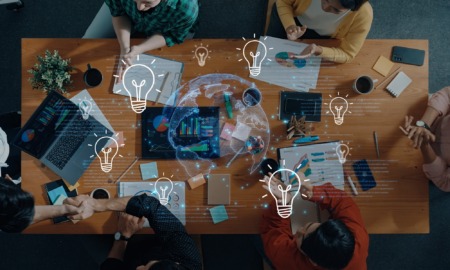 Educational leadership innovation grants: top-down view of group of people collaborating at table with lightbulb and globe graphics overlaid