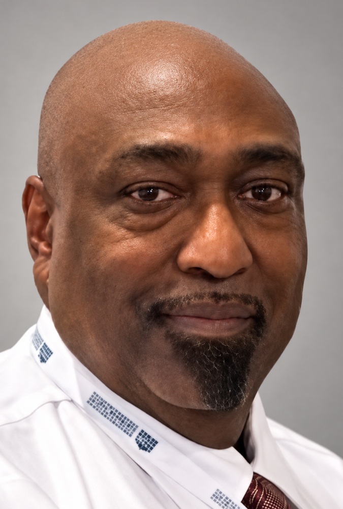 John Ginwright headshot: black, blad man in white collared shirt in front of grey background