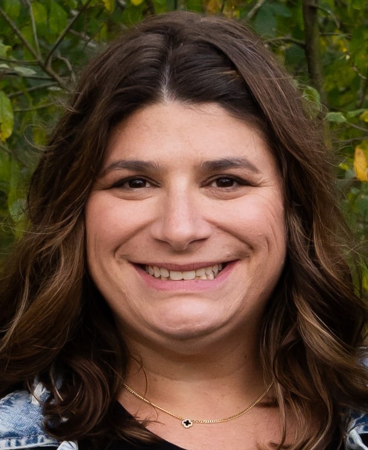 Lauren Nash headshot: woman with long dark hair smiling in front of greenery