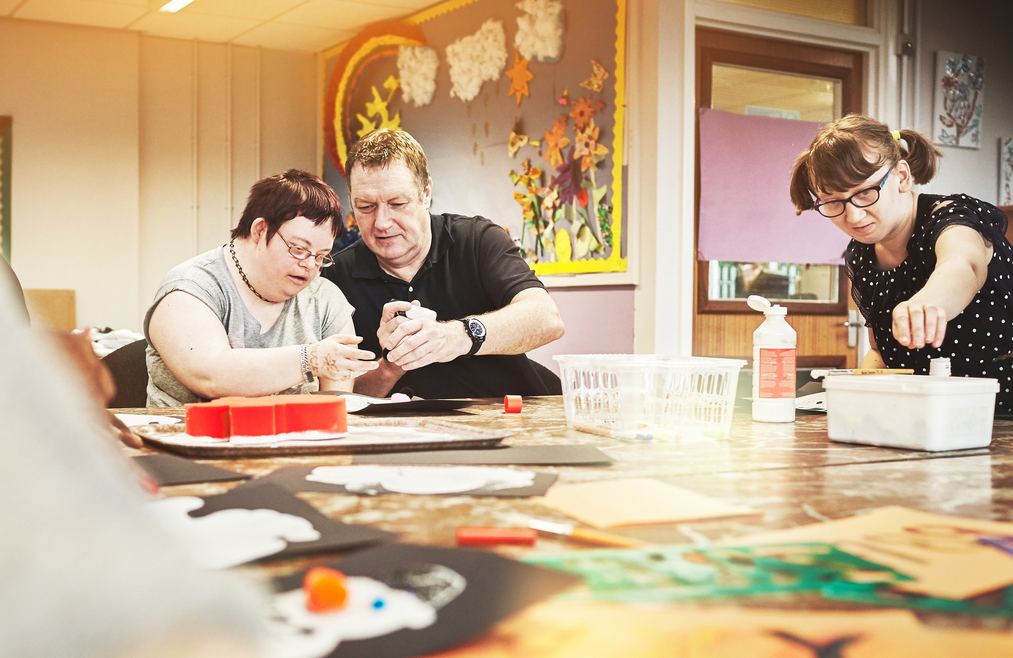 disability-informed mentorship for youth with disabilities should be a right, not a matter of chance_feature: an older man helps a young disabled person at table with task while another disabled person works on their own