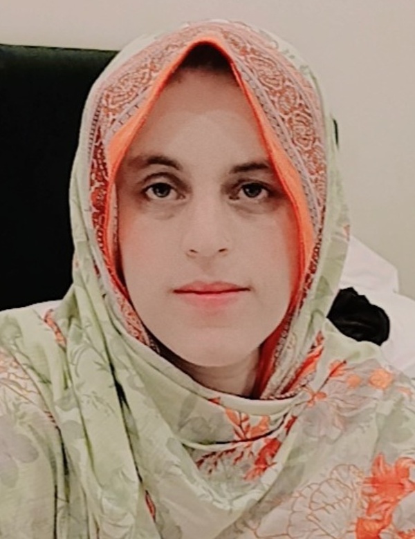 Shabina Badar headshot: woman in Muslim head scarf sitting indoors
