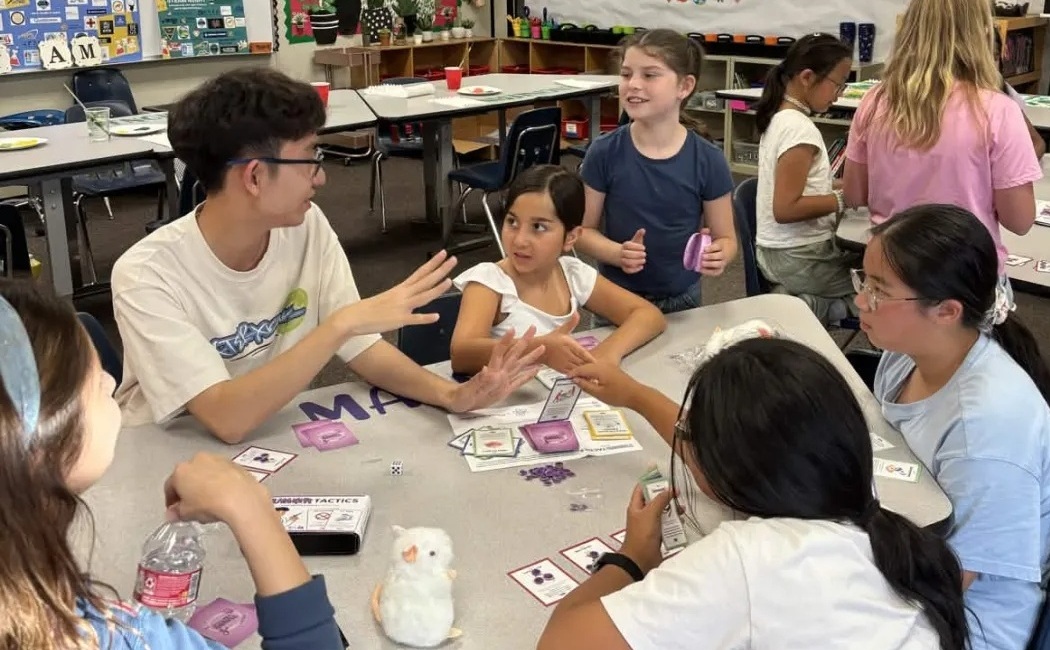 Students don’t just belong in STEAM classrooms-They belong at the front of them_Deer Canyon Workshop2: group of young students doing a workshop at a table being led by young Asian man