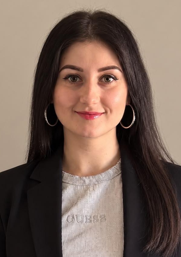 Hanna Kotyk headshot: white woman with long dark hair wearing black blazer and light t-shirt