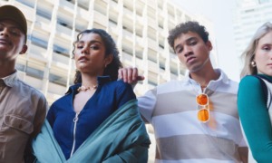 SYSTEM-INVOLVED YOUTH: FOUR TEENS WITH SERIOUS LOOKS ON THEIR FACES STAND NEXT TO EACH OTHER OUTSIDE IN FRONT OF A WHITE SKYSCRAPER